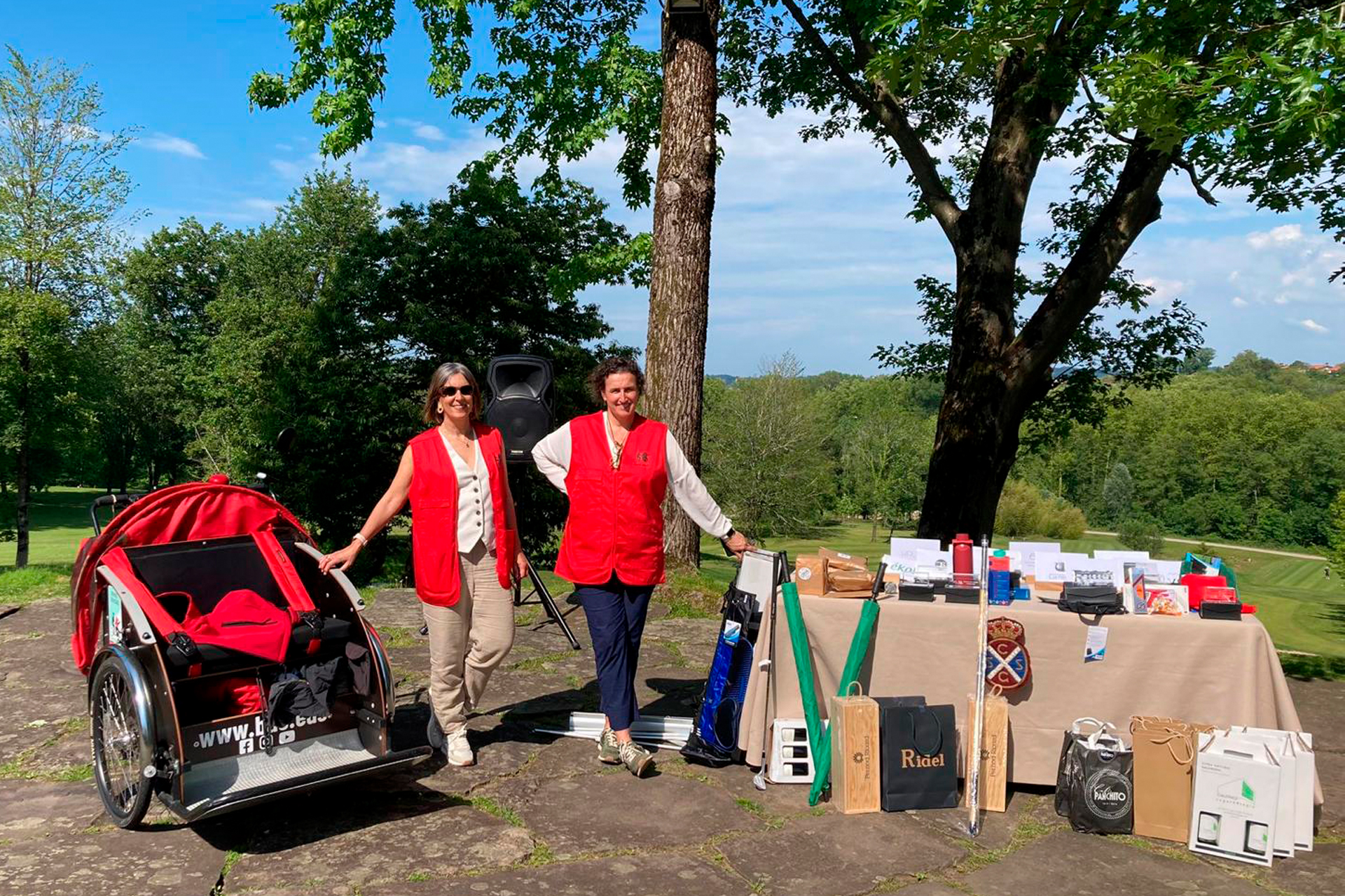 Voluntarias de BAE junto a un triciclo y una mesa con premios, en un campo de golf