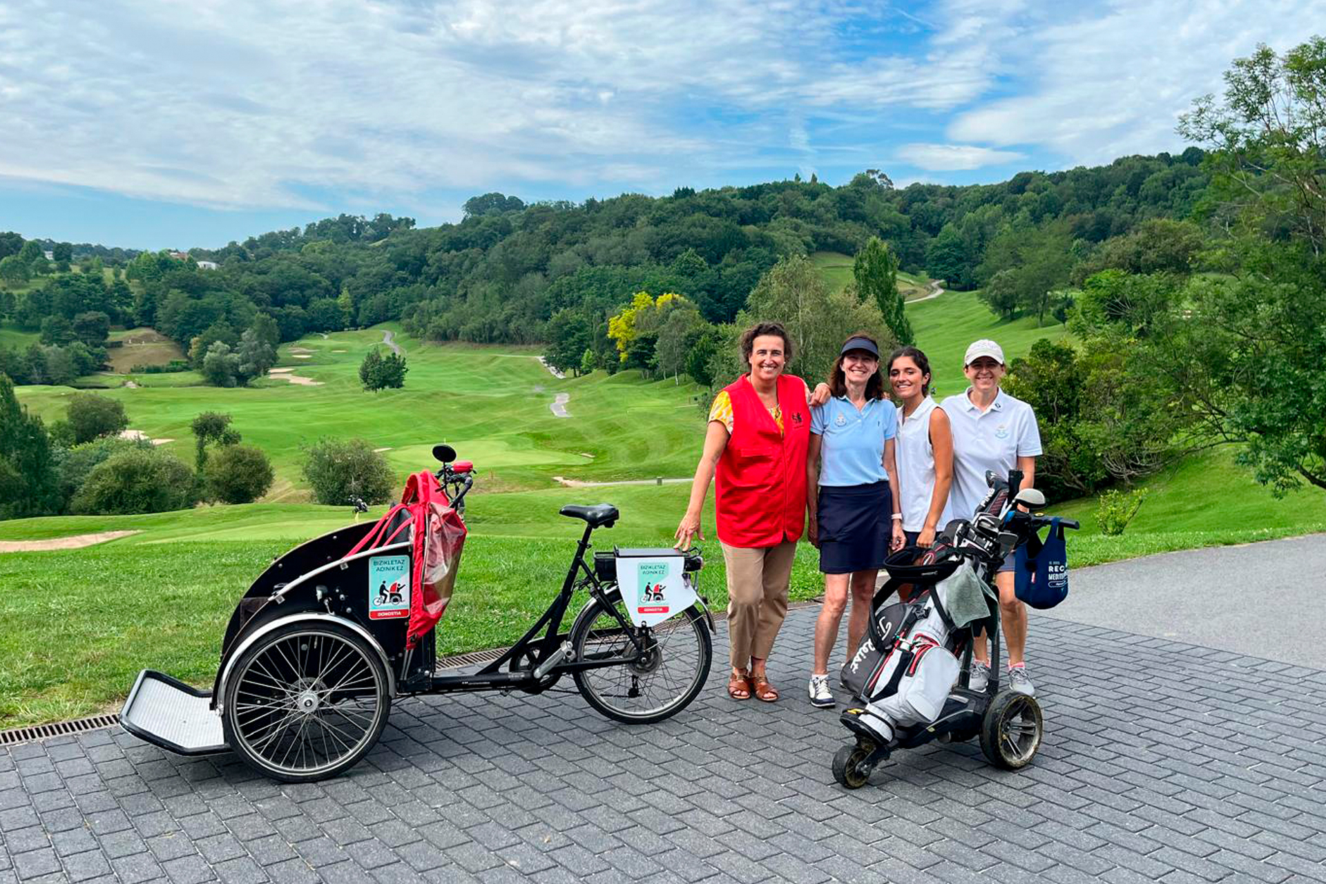 Grupo de personas junto al triciclo y con indumentaria de golf, en un campo de golf