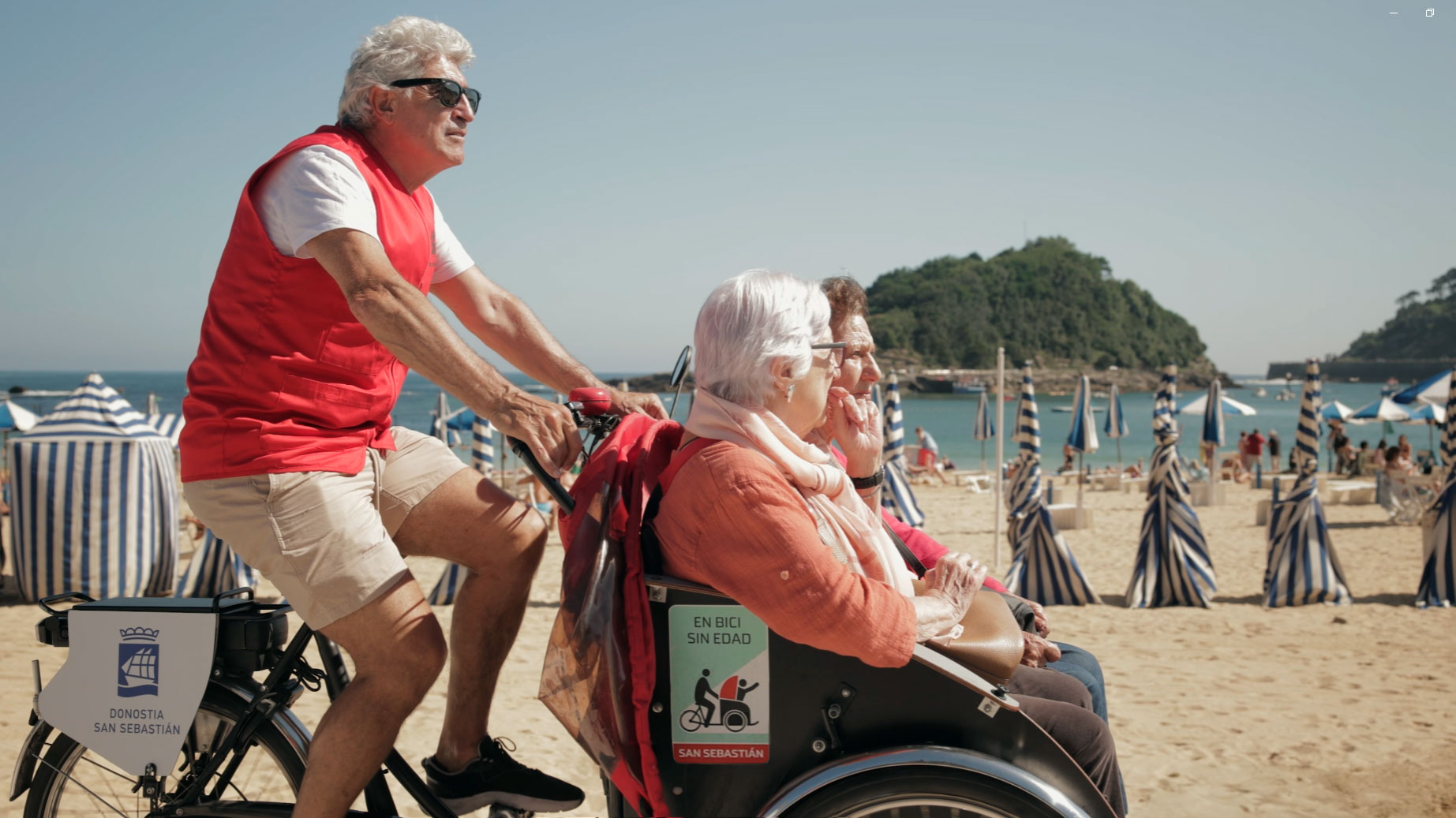 Un hombre pilotando un triciclo, con dos mujeres como pasajeras, frente a la playa
